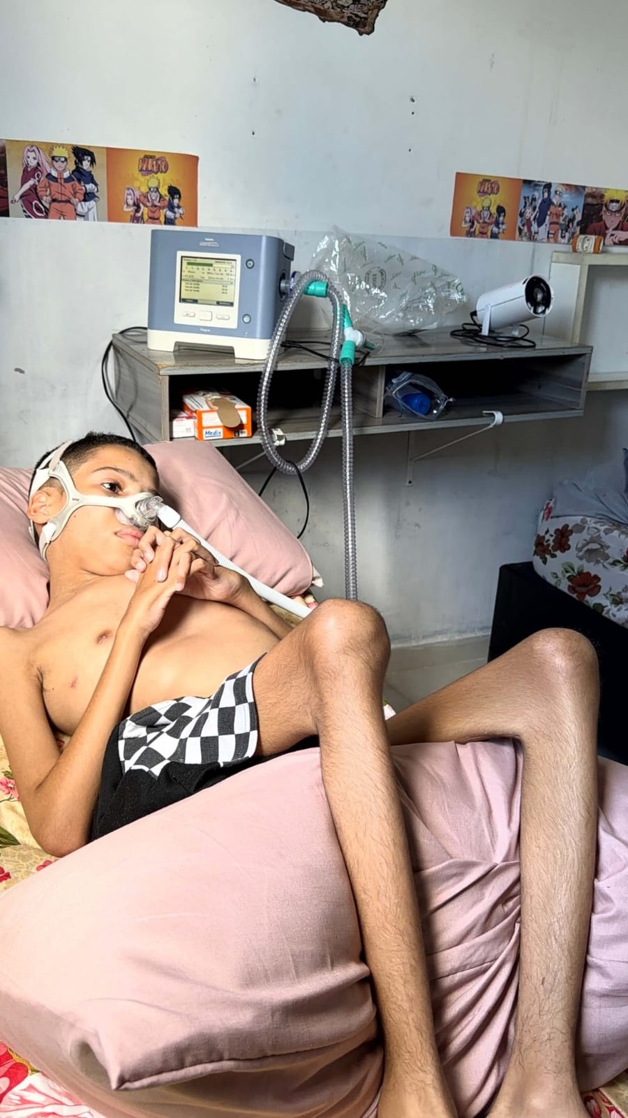 Kauê no quarto com o aparelho de respiração ao fundo